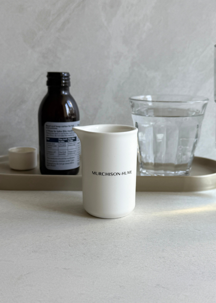 Ceramic measuring cup with medicine bottle and glass of water
