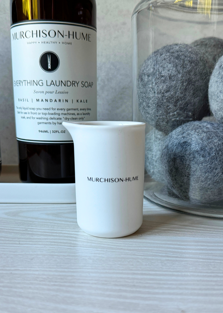 White ceramic measuring cup with precision markings next to Murchison-Hume laundry soap bottle